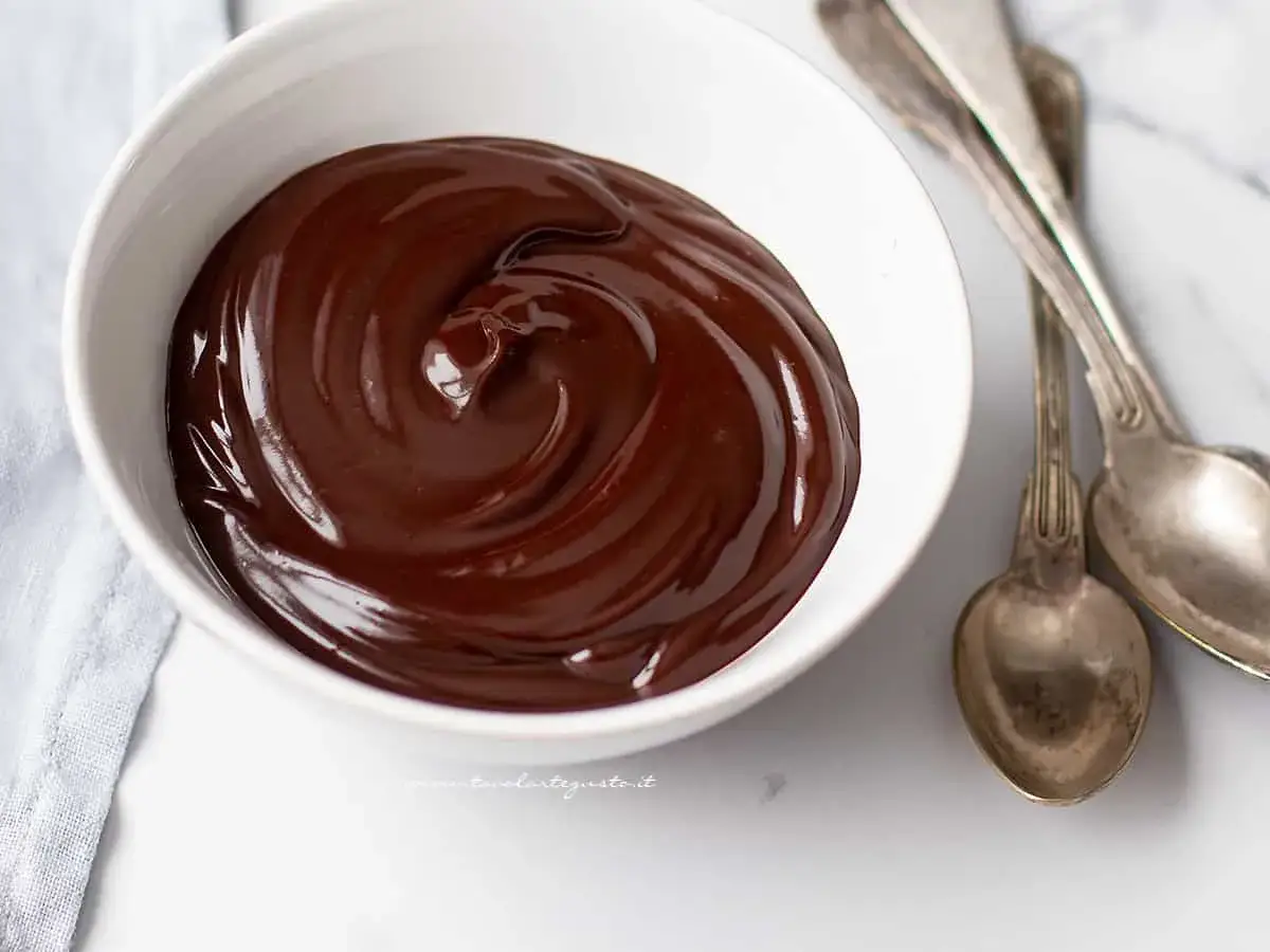 Una ciotola bianca piena di lucida glassa al cioccolato veloce, pronta per essere gustata con due cucchiai d'argento.