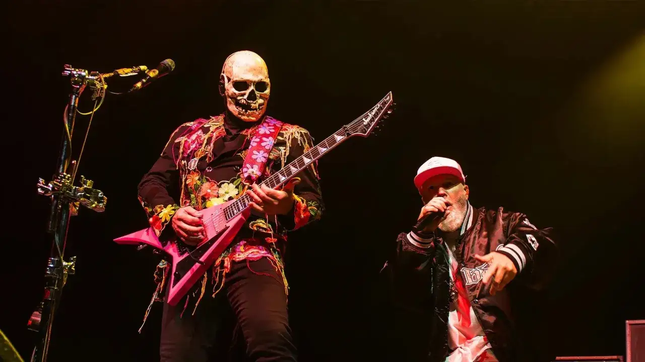 Muzyk w masce czaszki gra na r&oacute;żowej gitarze, a wokalista w czapce śpiewa na scenie podczas **impact festival**.