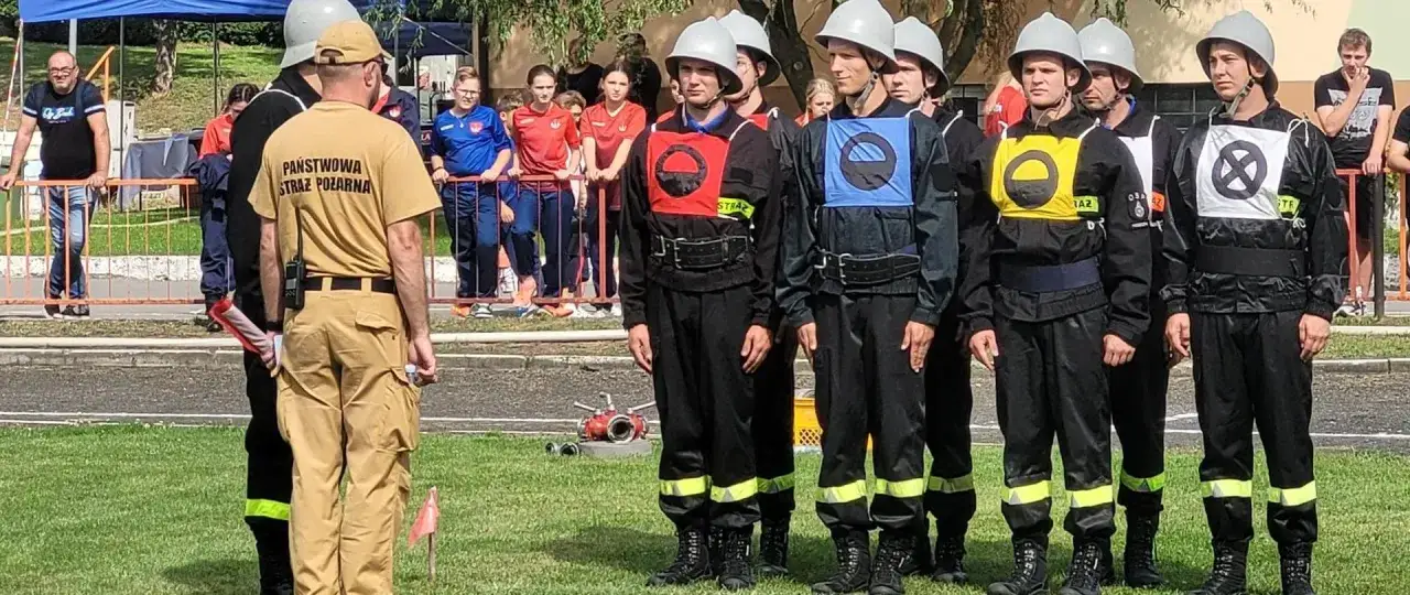 Młodzi strażacy w hełmach i kamizelkach biorą udział w zawodach OSP bojówka.
