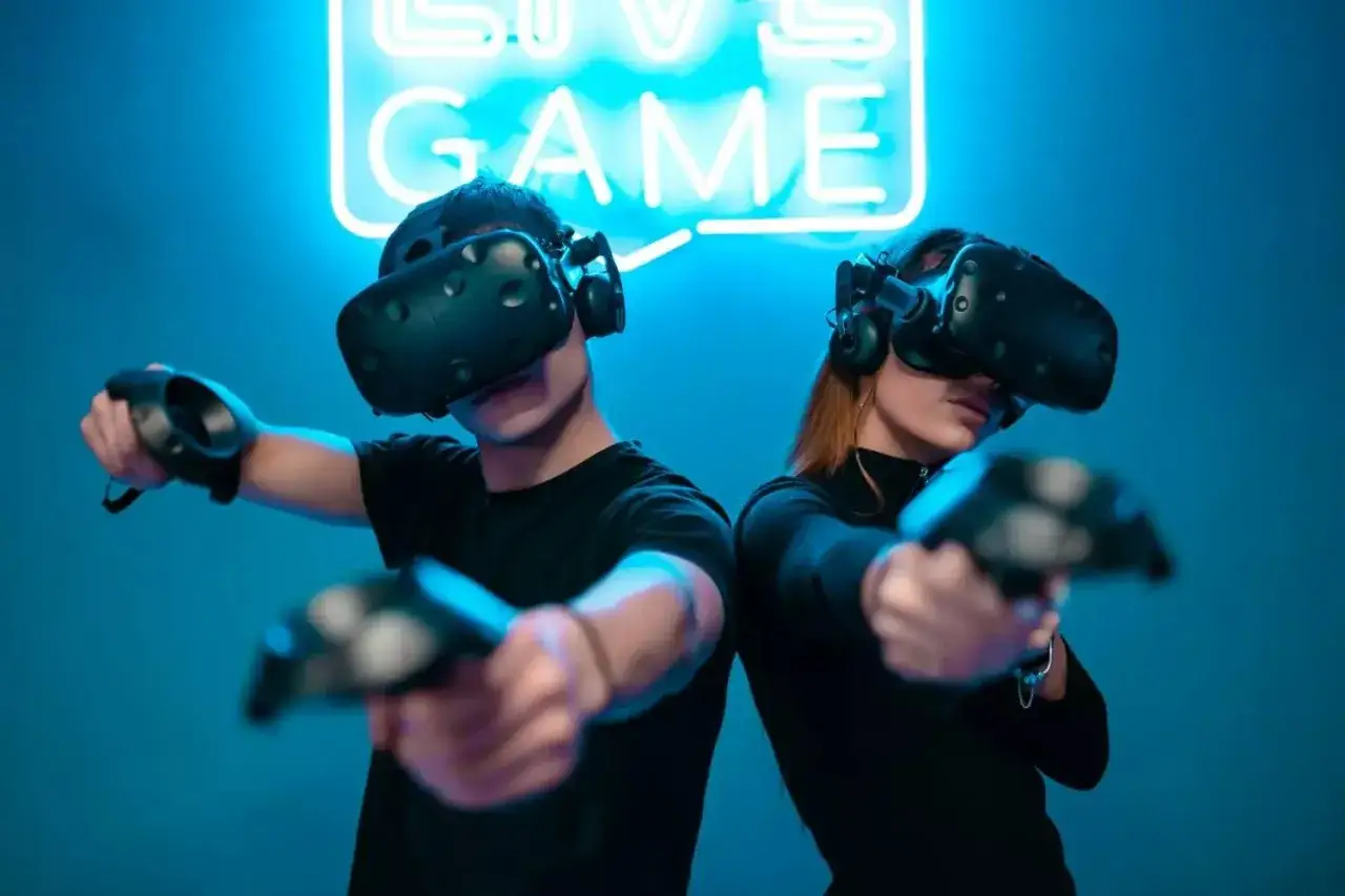 Para grająca w darmowe gry VR, z kontrolerami w dłoniach, pod neonowym napisem