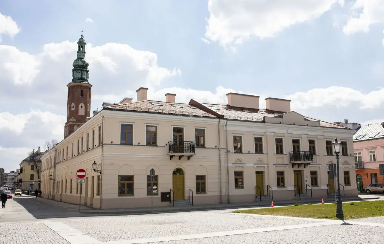 Radom atrakcje: zabytkowa kamienica z wieżą w tle, brukowany plac i błękitne niebo z chmurami.