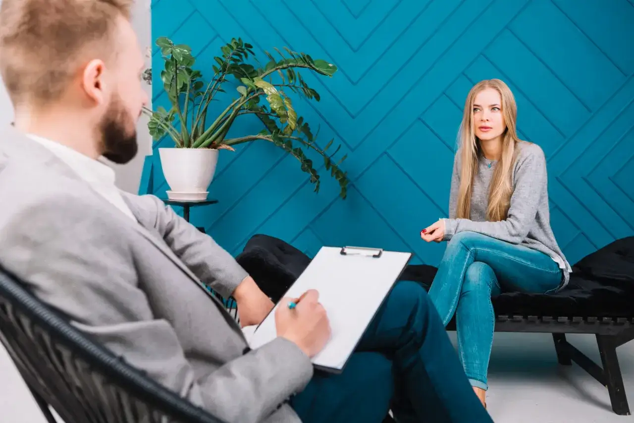 Mężczyzna z notatnikiem i długopisem prowadzi rozmowę z kobietą. To ich wizyta u psychiatry.
