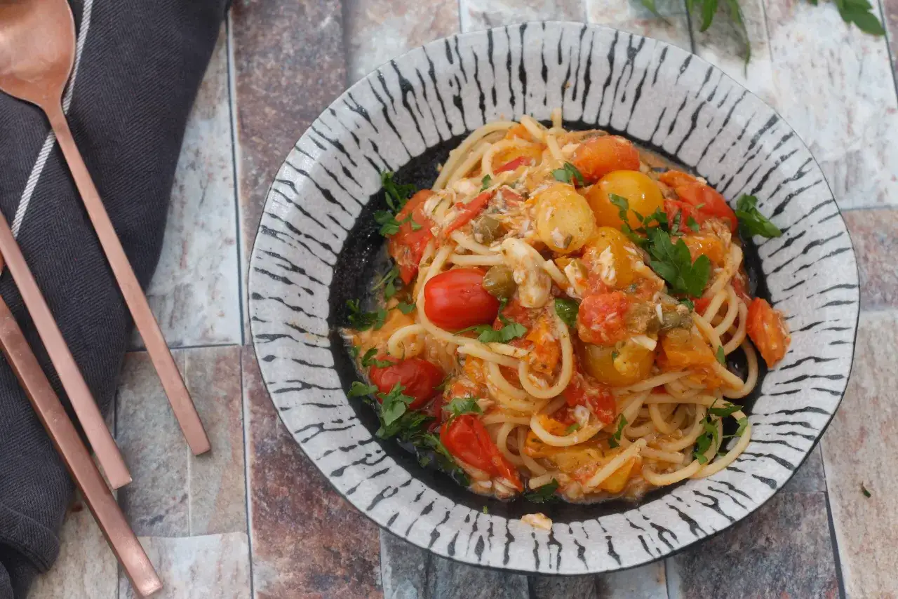 Spaghetti con pomodorini, capperi e un tocco di gallinella di mare, guarniti con prezzemolo fresco.