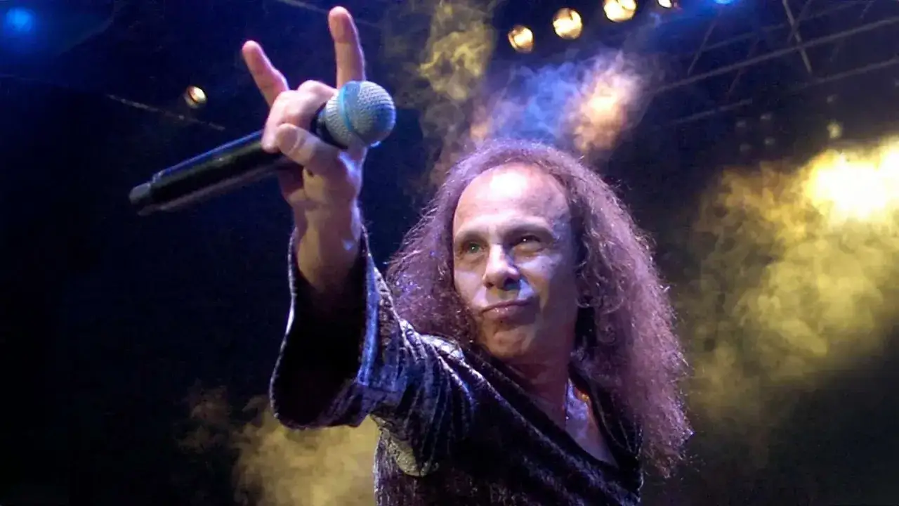 Ronnie James Dio, icona heavy metal, saluta il pubblico con il segno delle corna. La sua voce potente ha segnato generazioni, un'eredità che sfida la morte.
