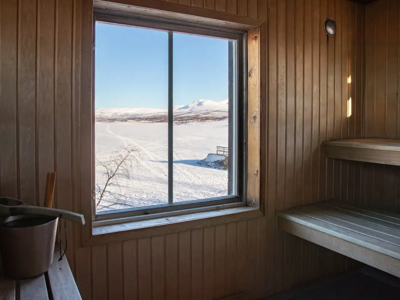 En mysig bastu med utsikt över ett snötäckt landskap. En skopa och hink står redo för ett bastubad som är nyttigt för både kropp och själ.