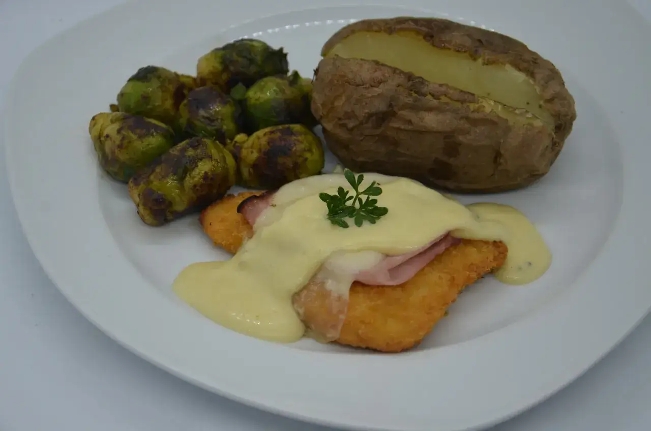 Escalope de poulet pané, jambon, fromage fondu et sauce au bleu, accompagné de choux de Bruxelles rôtis et d'une pomme de terre au four.