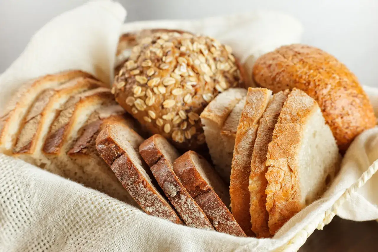 Koszyk pełen świeżego pieczywa, w tym bochenek z płatkami owsianymi. Idealny wybór, jeśli zastanawiasz się, jaki chleb nie ma glutenu.