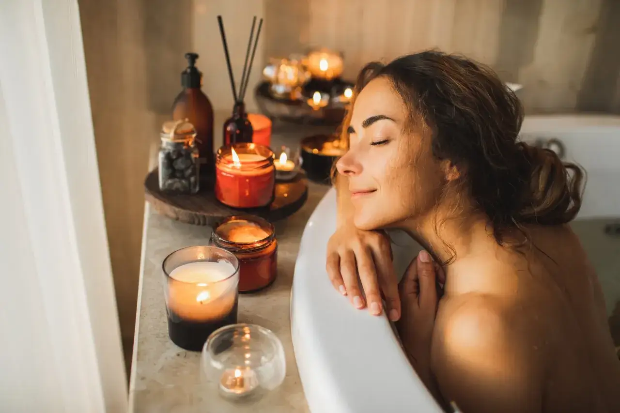 Mujer disfrutando de un baño relajante, rodeada de velas encendidas y aromas.