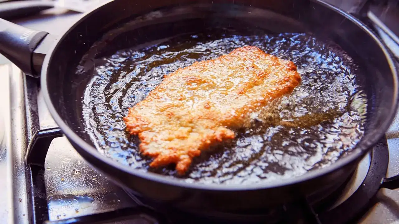 Ein goldbraunes Putenschnitzel braten in heißem Öl in einer Pfanne. Es zischt und dampft, die Kruste wird knusprig.