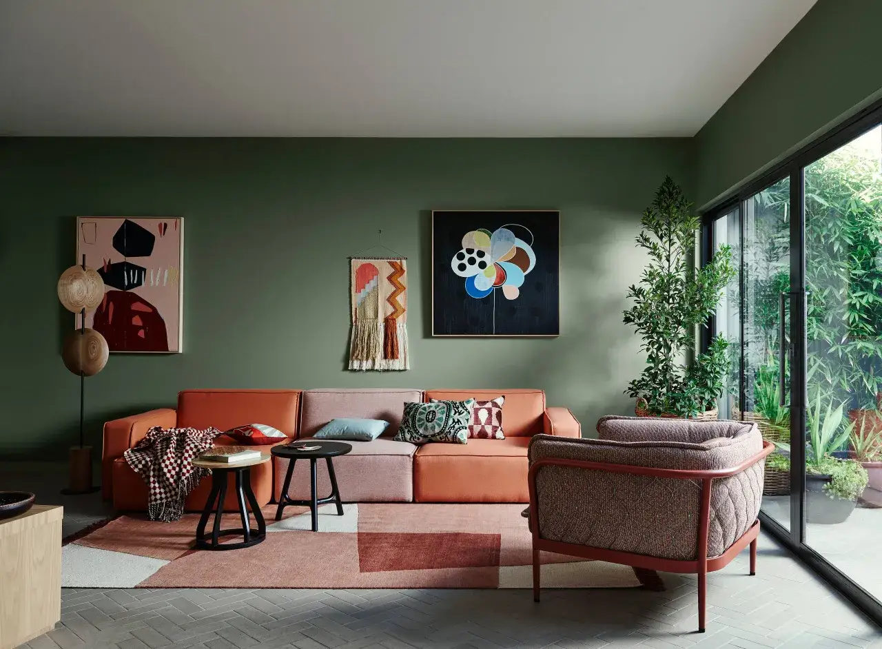 Grüne Wandfarben sind modern und schaffen eine beruhigende Atmosphäre. Ein orangefarbenes Sofa und bunte Kissen setzen Akzente.