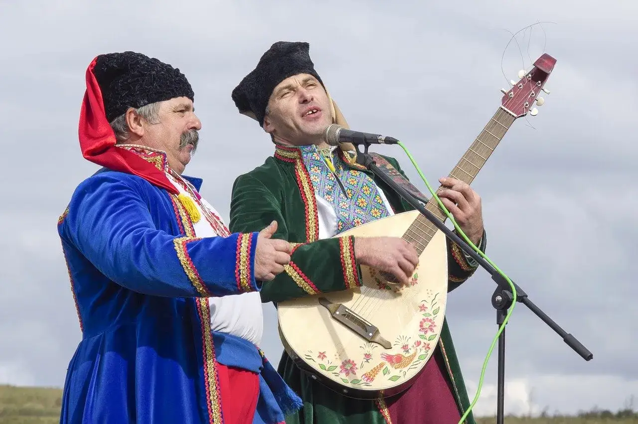 Dwóch mężczyzn w tradycyjnych strojach, jeden gra na mandolinie, drugi śpiewa. Występ artystyczny mniejszości etnicznych w Polsce.