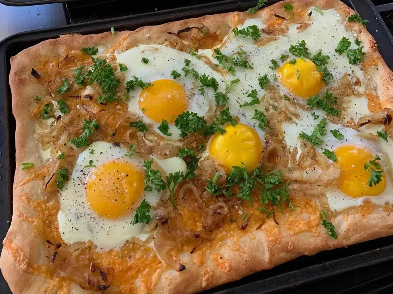 Pyszna pizza z jajkiem, cebulą i serem, posypana świeżą natką pietruszki. Idealna na śniadanie lub brunch.