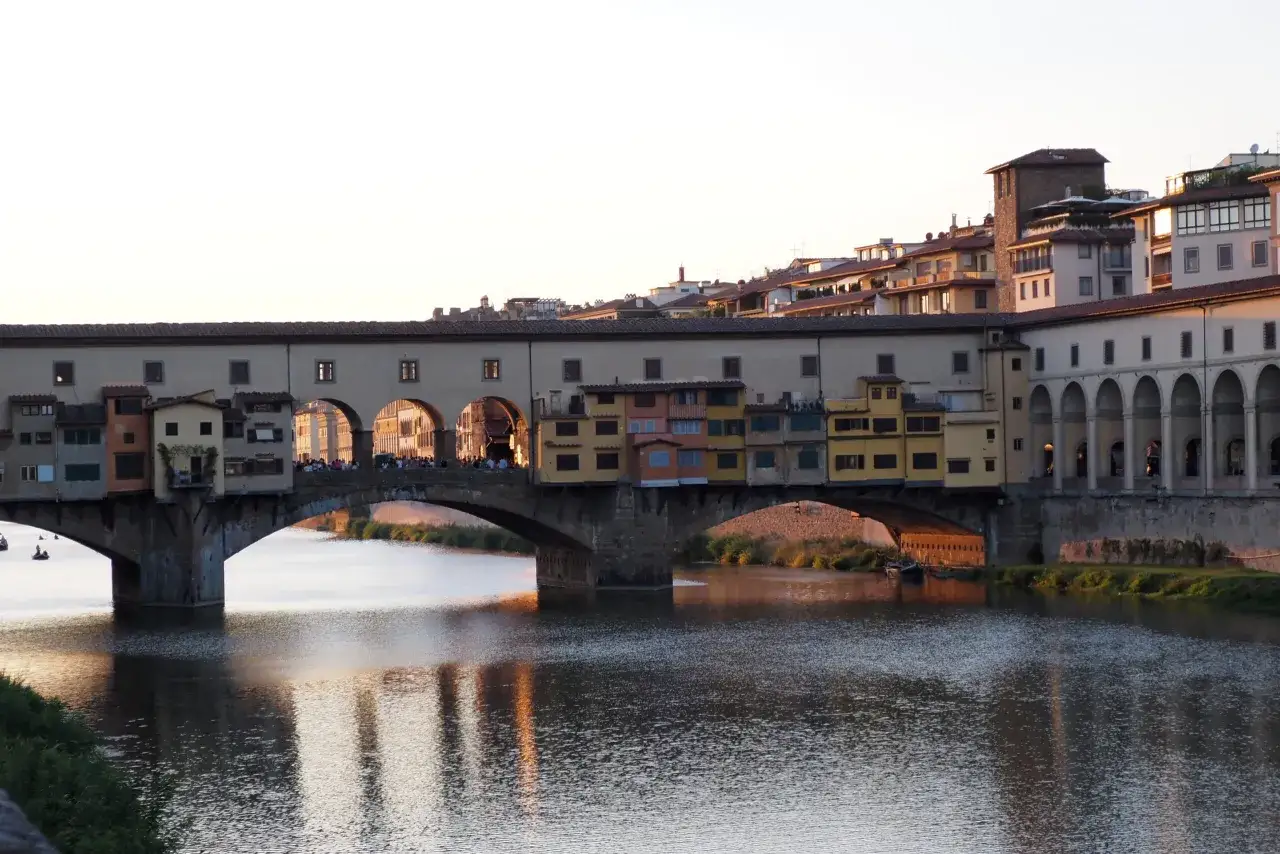 Mostra Ponte Vecchio we Florencji, idealne miejsce do zobaczenia podczas zwiedzania miasta. Woda rzeki Arno odbija ciepłe światło zachodzącego słońca.
