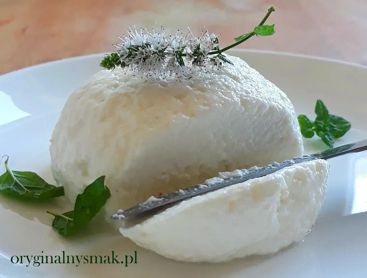Puszysta, domowa ricotta ozdobiona kwiatami mięty, z nożem wbijanym w ser.
