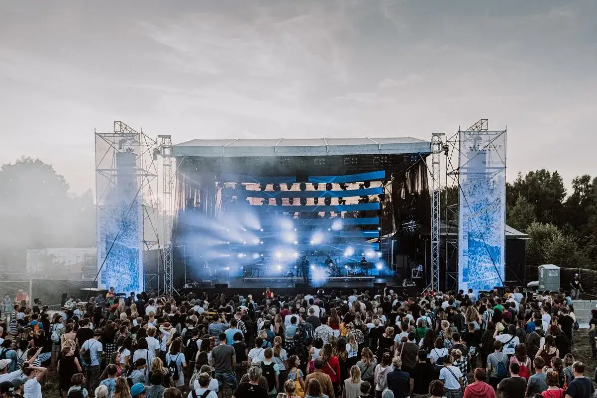 Tłumy ludzi na koncercie podczas jastarnia festiwal. Na scenie gra zespół, a nad publicznością unosi się mgła i światła.