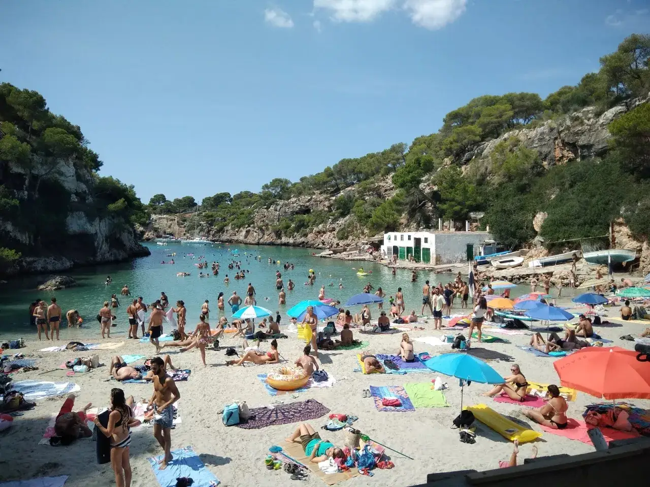 Folk njuter av solen och badar i det turkosa vattnet vid Cala Pi. En livlig stranddag med m&aring;nga bes&ouml;kare.