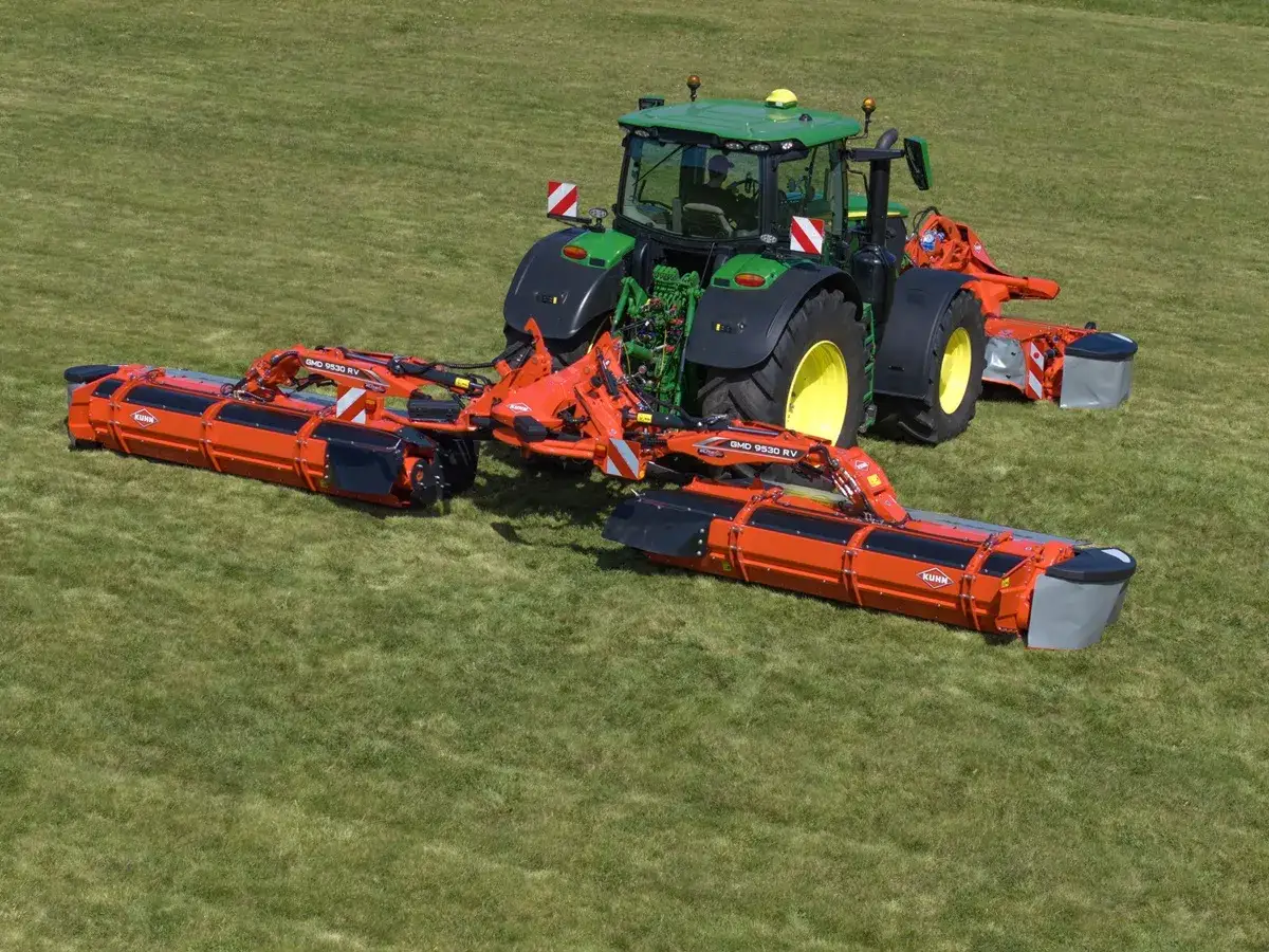 Zielony traktor z dwoma pomarańczowymi kosiarkami dyskowymi Kuhn GMD 9530 RV na zielonej łące.