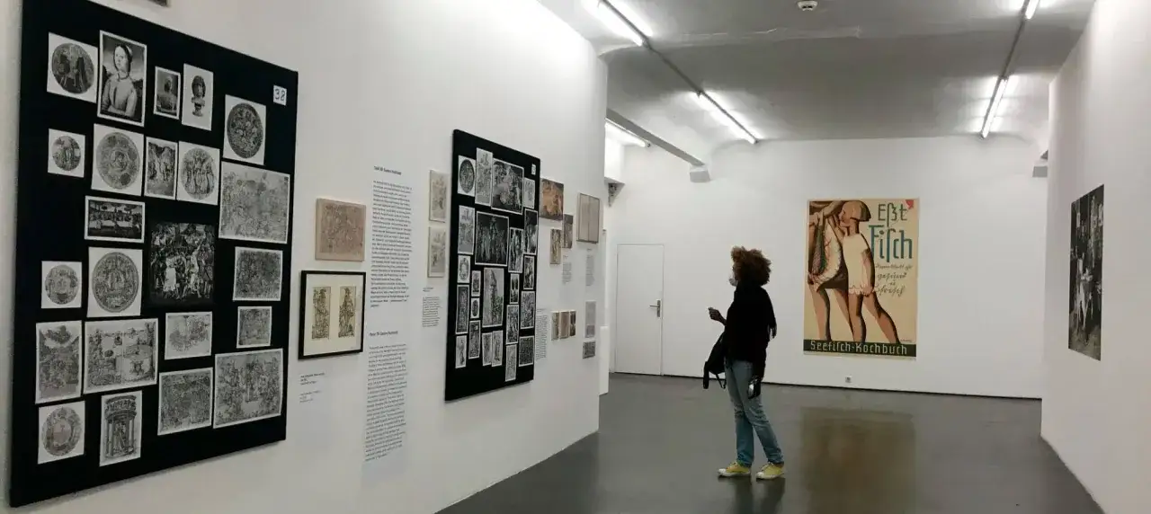 Besucherin betrachtet Kunstwerke in einer Galerie. Die foto messe hamburg zeigt eine Frau, die sich vor einer Wand mit vielen Bildern und einem Plakat befindet.
