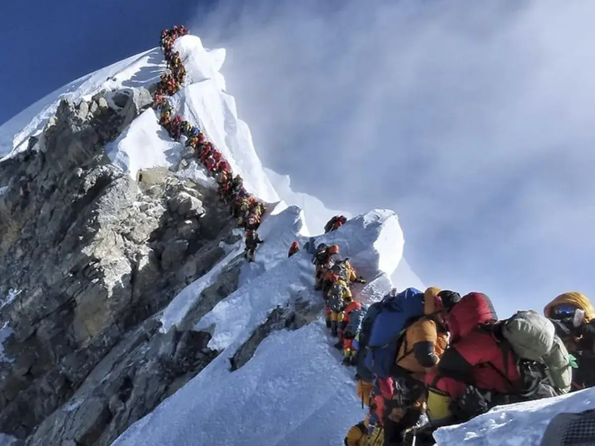 Korek na Mount Everest. Tłum ludzi w kolorowych kurtkach i z plecakami wspina się po ośnieżonym zboczu.