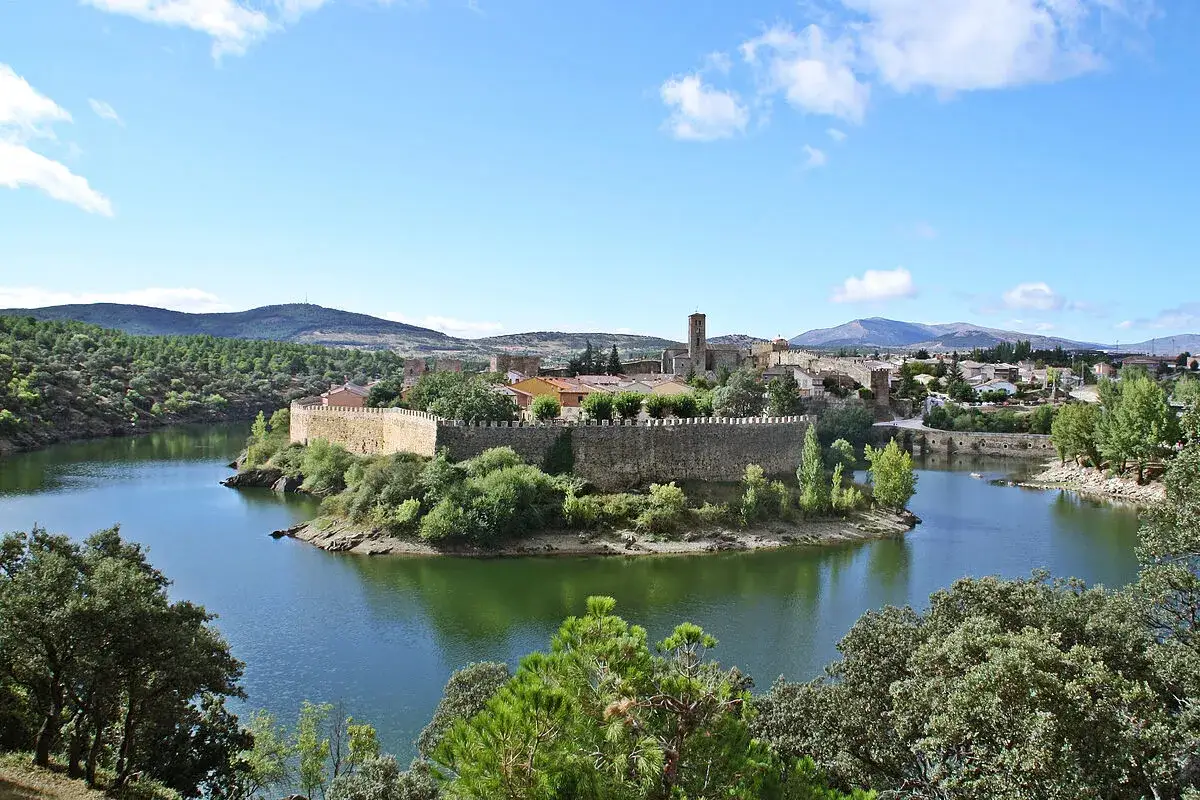 El pueblo amurallado de Buitrago de Lozoya se alza sobre un meandro del r&iacute;o, rodeado de vegetaci&oacute;n y monta&ntilde;as.