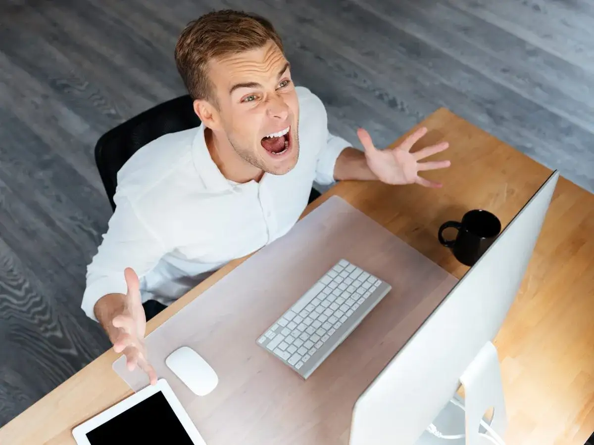 Uomo frustrato al computer, con le mani alzate in segno di disperazione. Un chiaro esempio di ambiente di lavoro tossico.