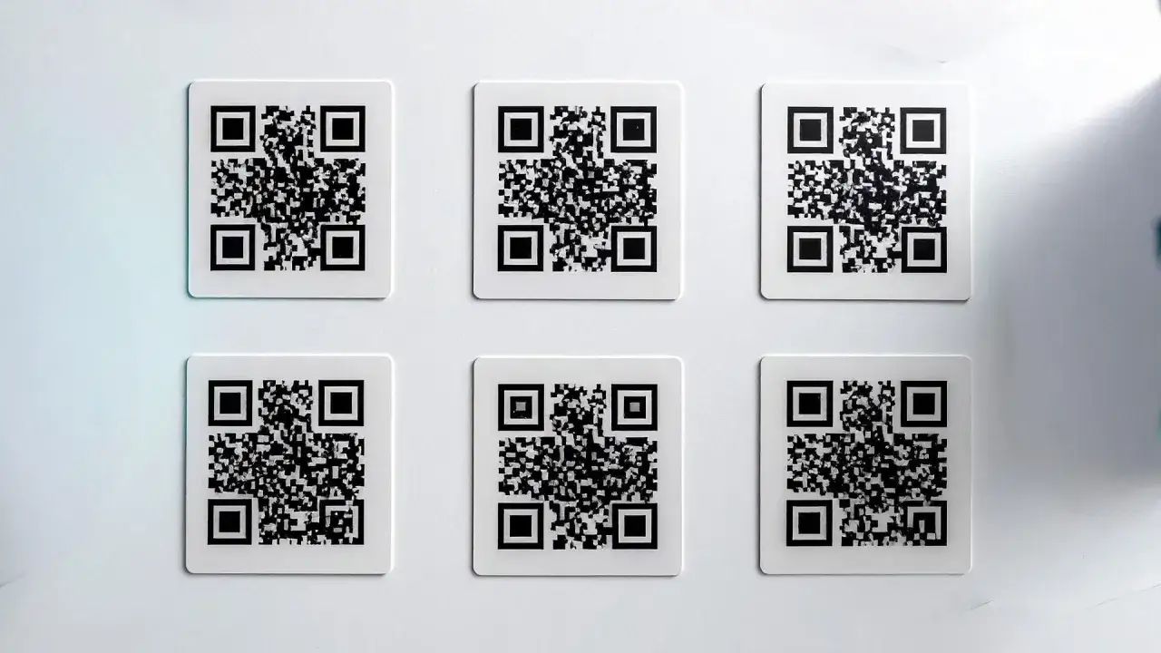 Sześć kwadratowych kodów QR na białej ścianie. Użyj aplikacji do sprawdzania oryginalności produktu, skanując je.