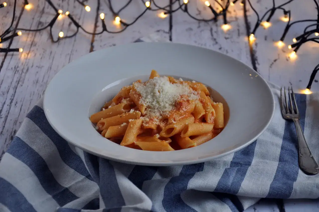 Penne alla vodka w kremowym sosie pomidorowym, posypane parmezanem, na tle świątecznych lampek.