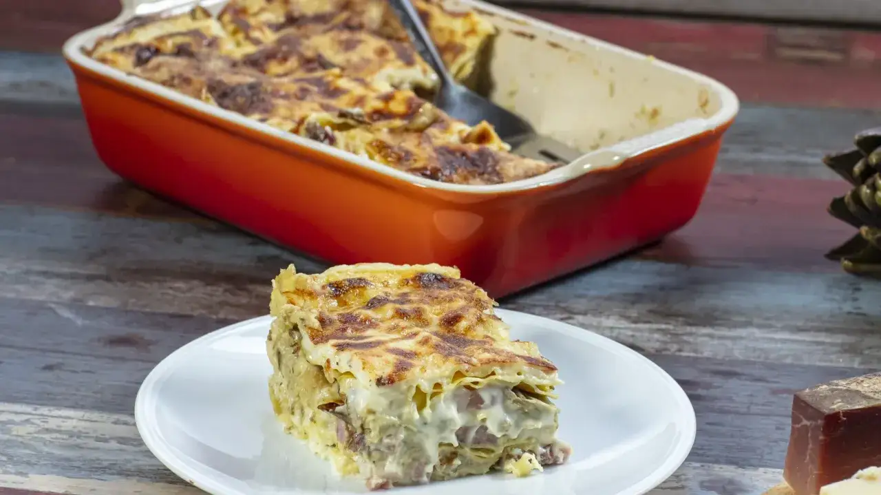 Una fetta di lasagne con carciofi surgelati, cremosa e dorata, servita su un piatto bianco.