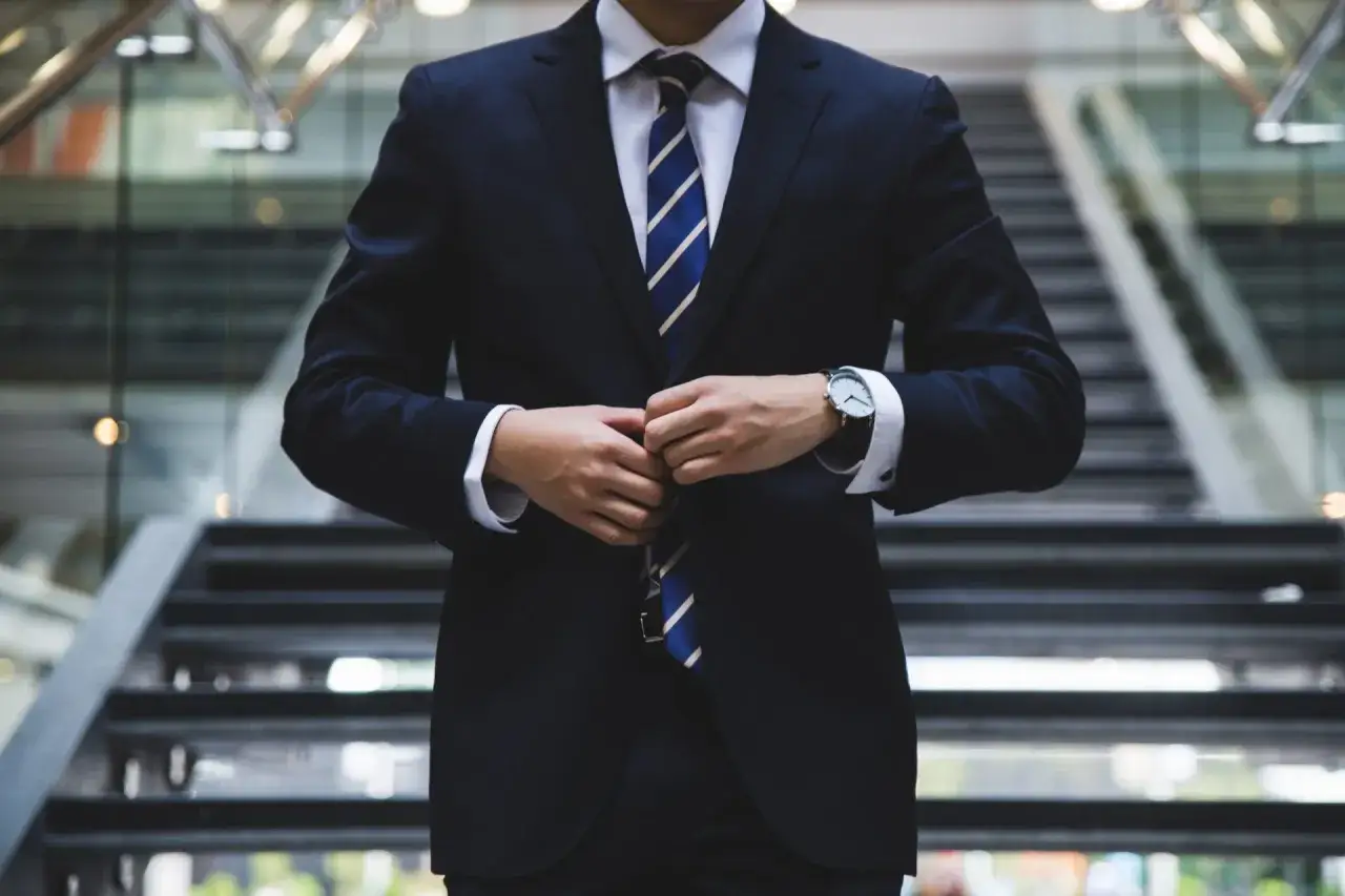 Mann im dunklen Anzug mit blau-weiß gestreifter Krawatte, der seinen blauen Blazer kombiniert.
