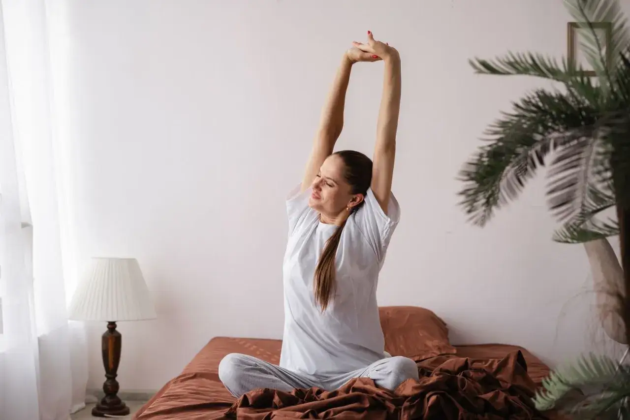 Une femme s'étire sur son lit, prête à commencer sa journée avec énergie, comme après un bon café et une dose de rhodiola.