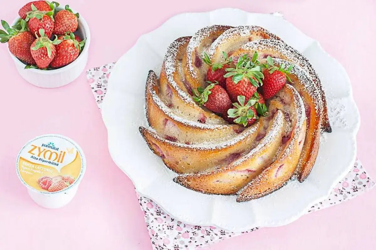 Torta di fragole e yogurt, soffice e profumata, decorata con zucchero a velo e fragole fresche.
