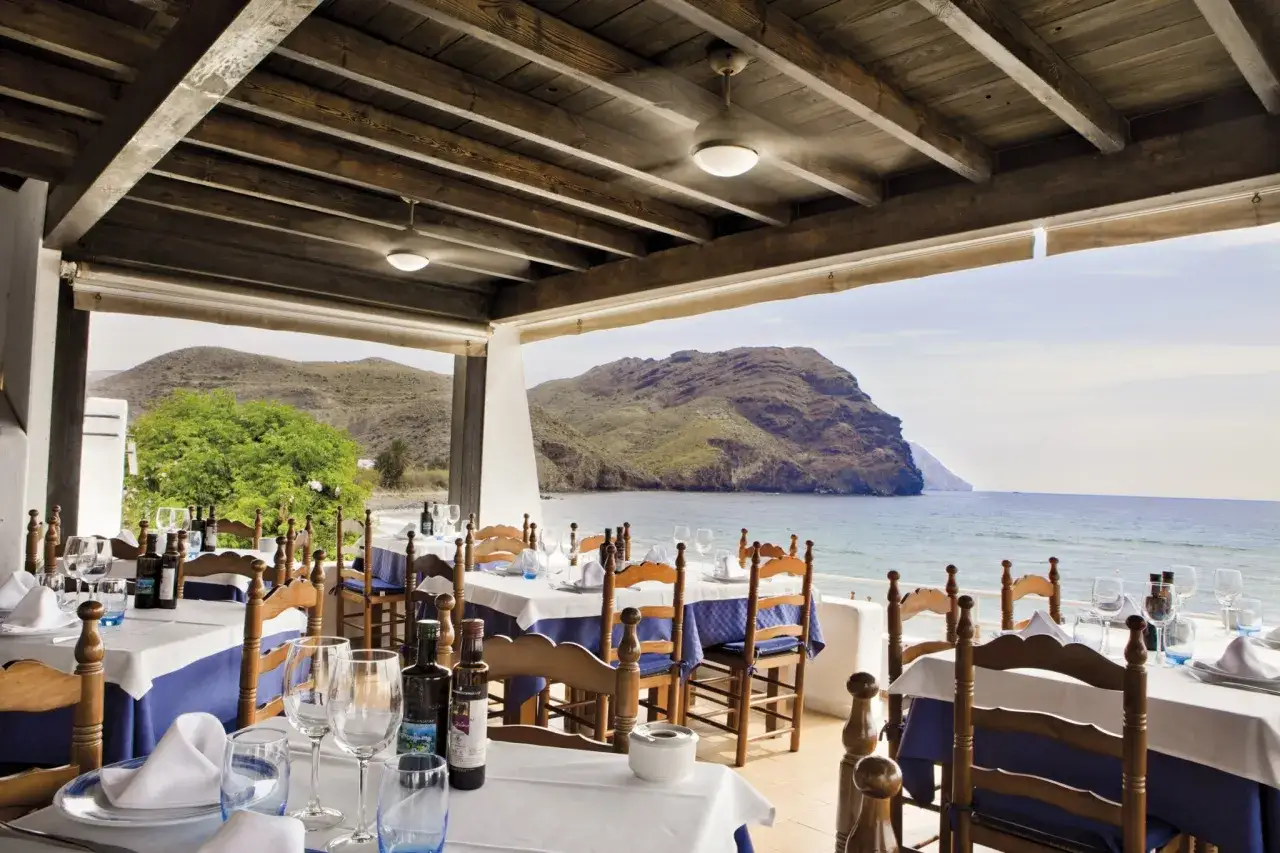 Mesas listas para cenar en un restaurante con vistas al mar. El manteca las negras, un aceite de oliva local, reposa en las mesas.