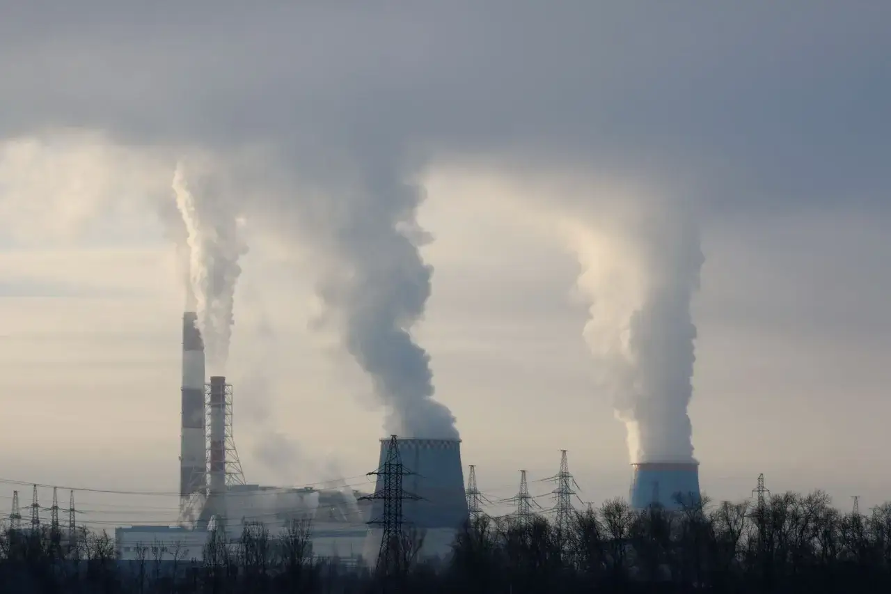 Dymiące kominy elektrowni, symbolizujące produkcję **coal energy**, unoszą się na tle pochmurnego nieba.