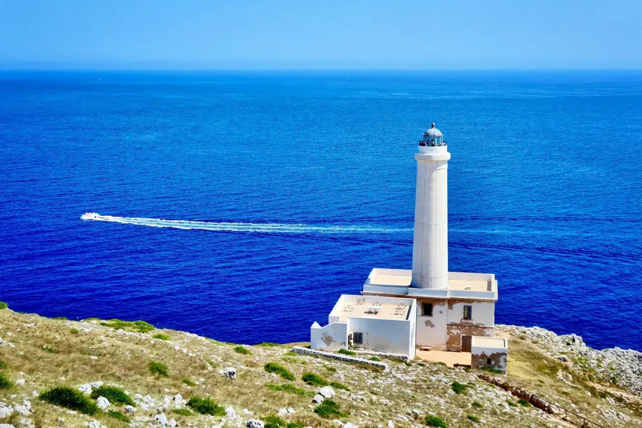 Faro di Punta Palascìa, uno dei luoghi da scoprire a Otranto, con il mare blu e una barca in lontananza.