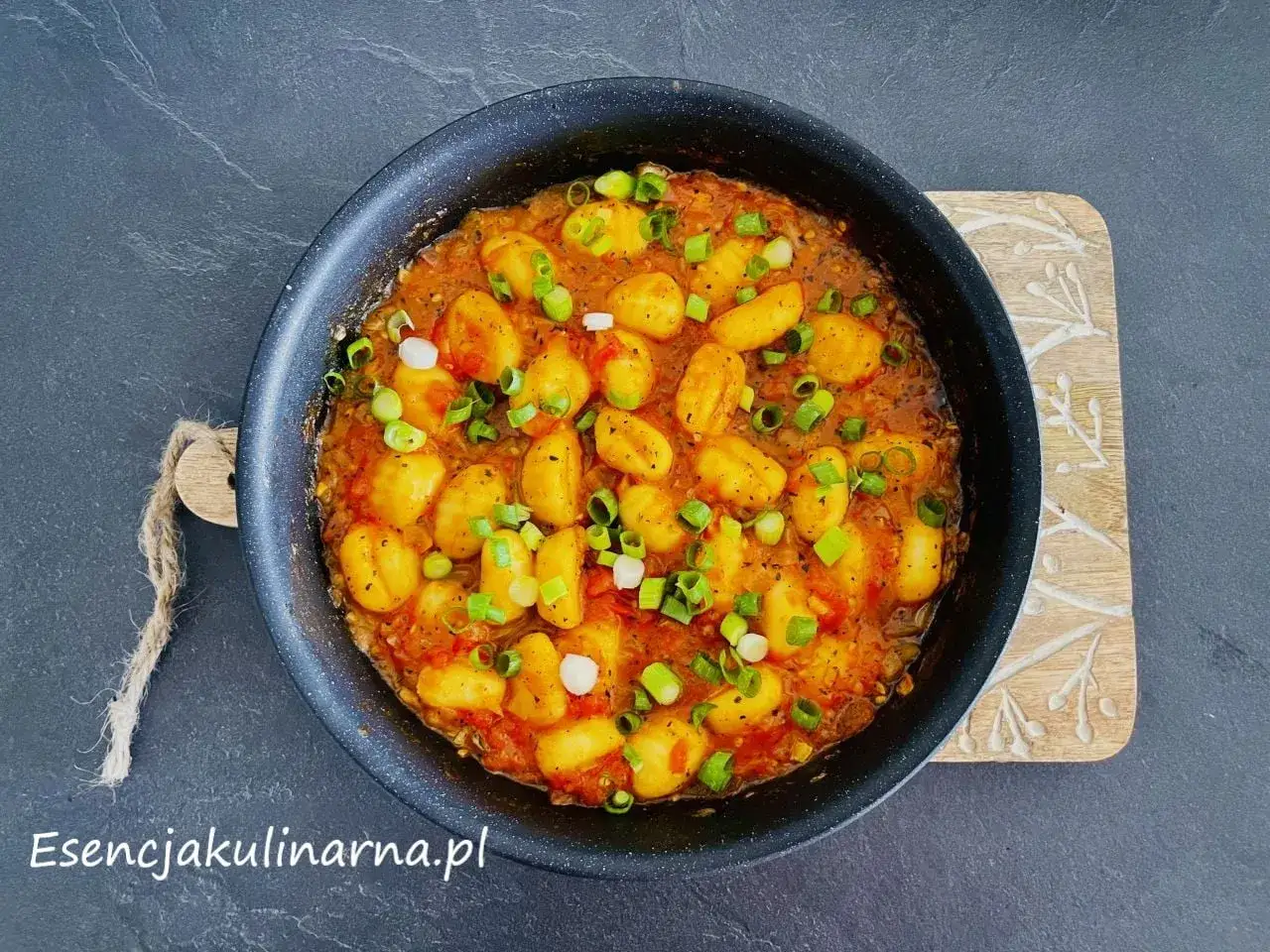 Pyszne gnocchi w sosie pomidorowym, posypane szczypiorkiem, podane w czarnej patelni.