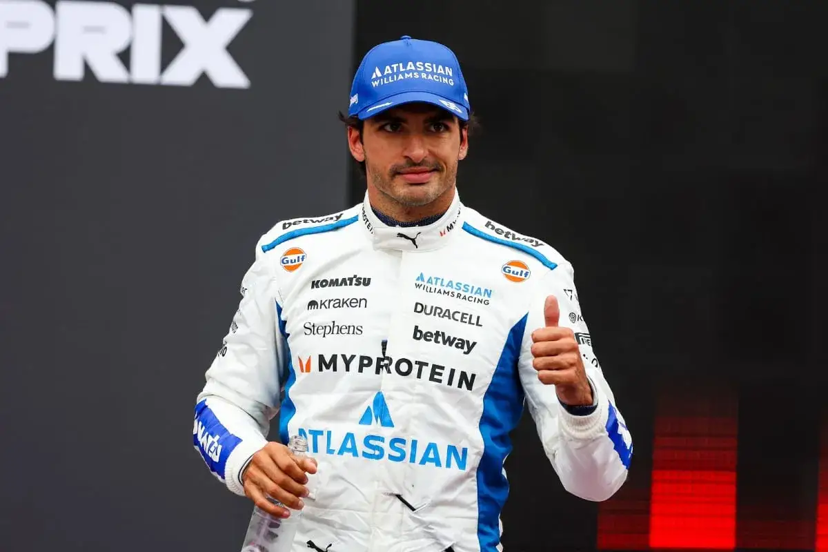 Carlos Sainz Jr. con gorra azul y mono blanco de Williams Racing, da pulgar arriba.