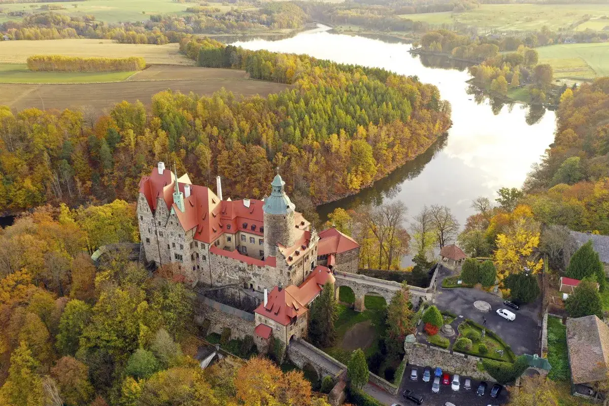 Zamek Czocha, gdzie jest, otoczony jesiennymi barwami, malowniczo położony nad rzeką.