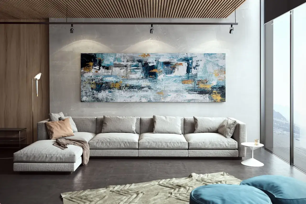 Un sal&oacute;n moderno con un gran sof&aacute; gris y unos impresionantes cuadros murales abstractos en tonos azules y dorados que capturan la luz.