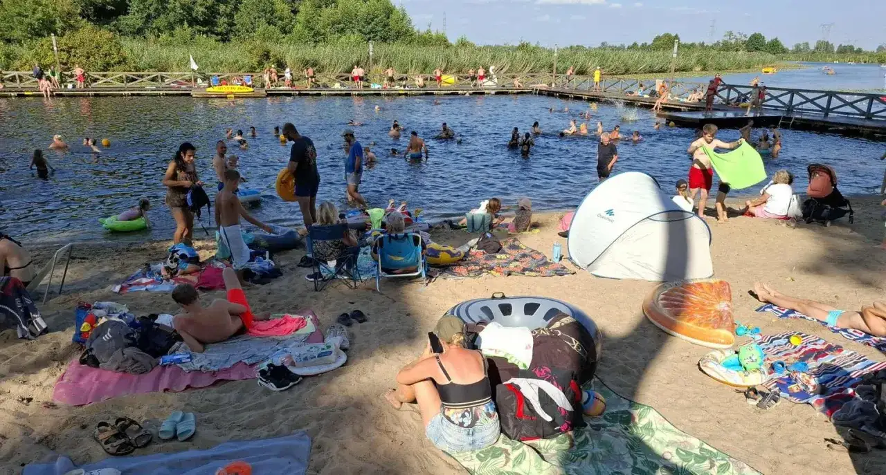 Ludzie odpoczywają i kąpią się nad **jeziorem kozienickim**. Słońce, plaża i woda tworzą idealne warunki do letniego relaksu.