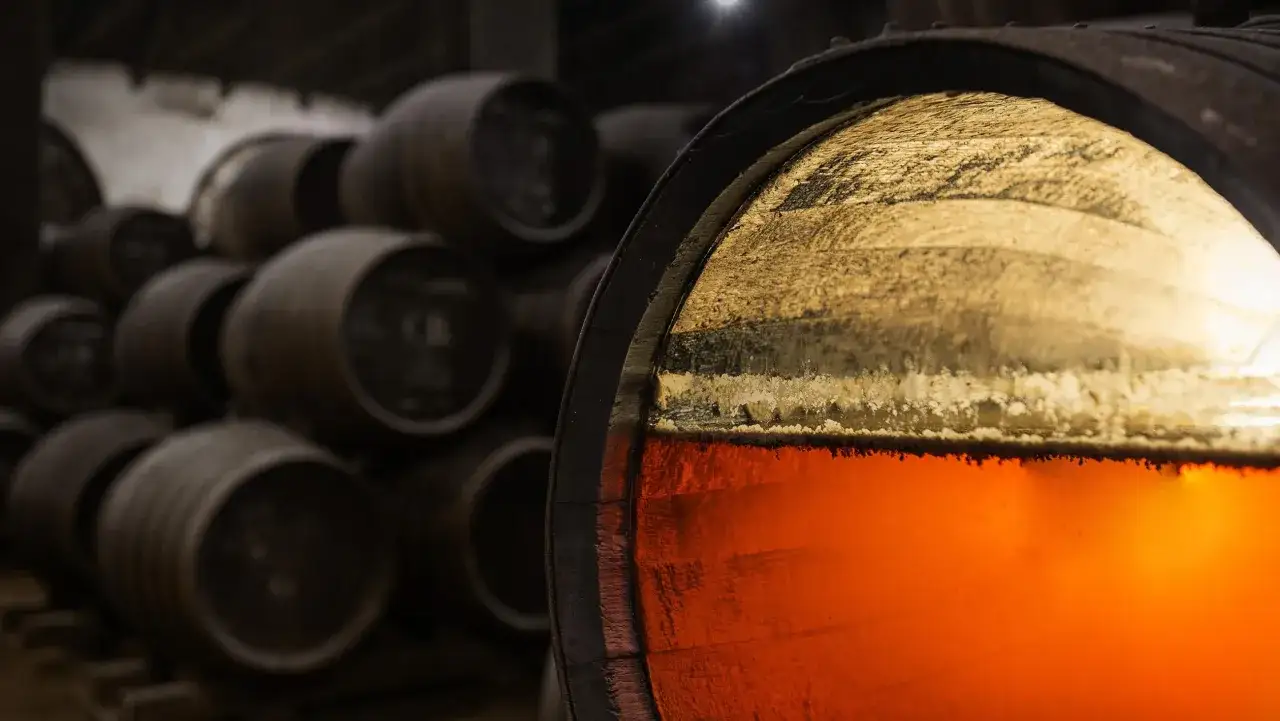 Ein Fass mit bernsteinfarbenem Sherry-Alkohol, daneben weitere Fässer in einem Lagerraum.