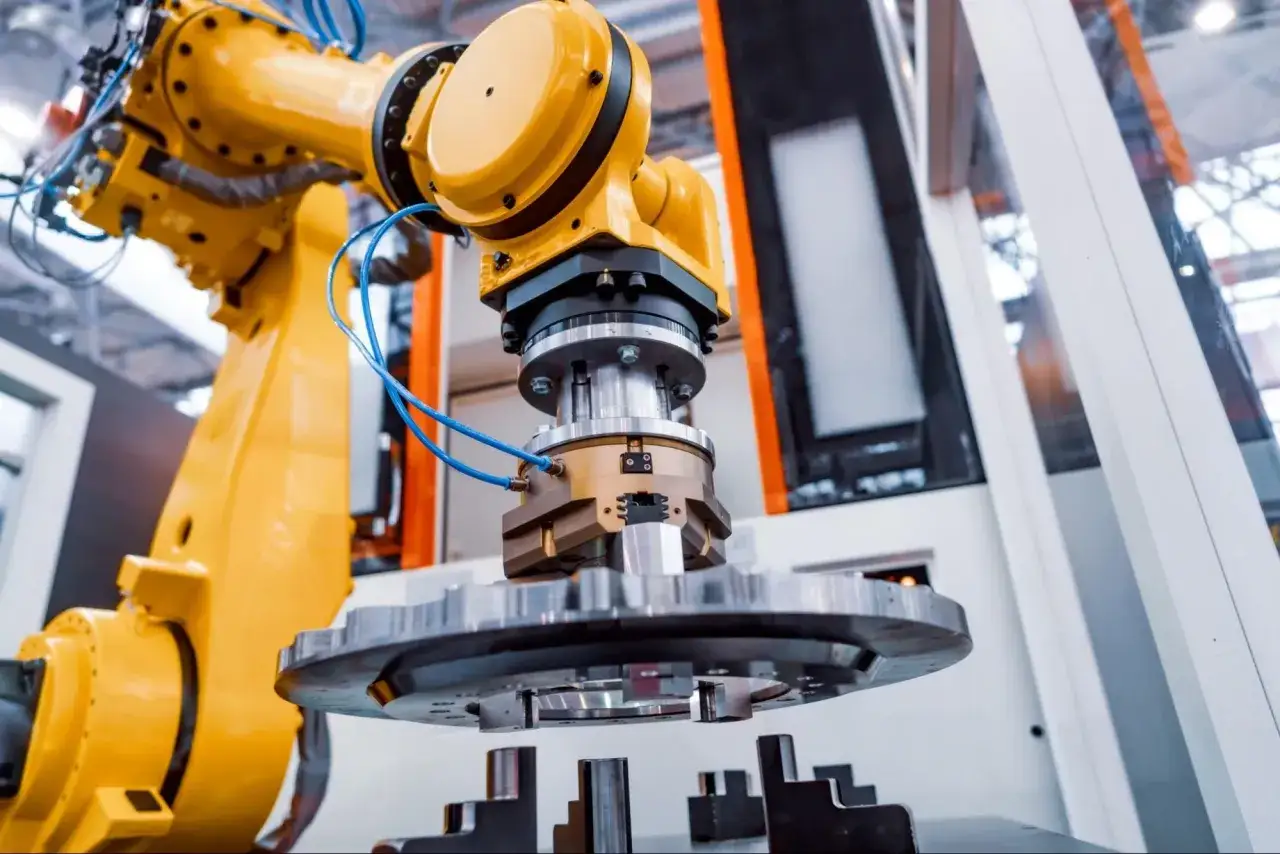 Żółty robot przemysłowy z chwytakiem, jeden z wielu rodzajów manipulatorów, precyzyjnie operuje metalowym elementem.