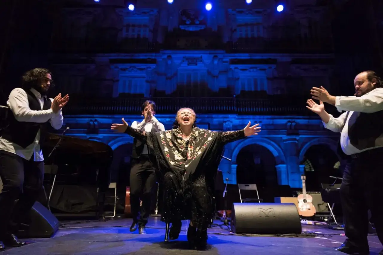 La Chana, icónica bailaora flamenca, canta con pasión en el escenario, rodeada de músicos.