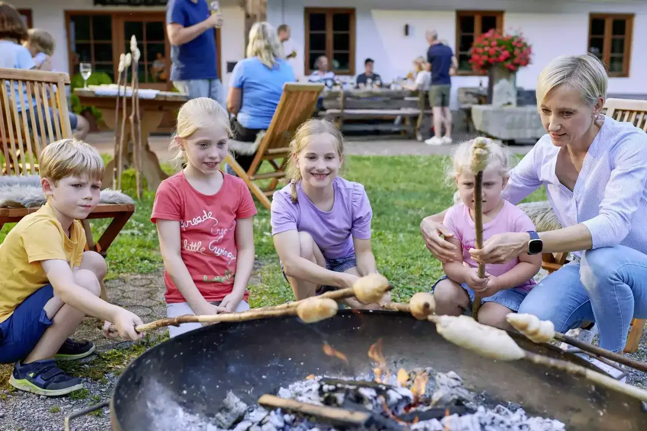Kinder und eine Frau backen Stockbrot ohne Hefe am Lagerfeuer. Ein fr&ouml;hlicher Familienmoment im Freien.