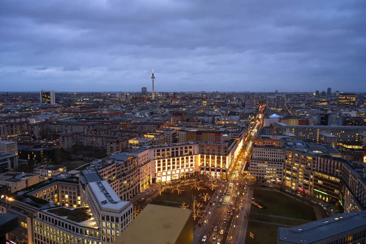 Dämmerung über Berlin. Der **Berliner Fernsehturm** ragt in den grauen Himmel, während die Stadtlichter zu funkeln beginnen.