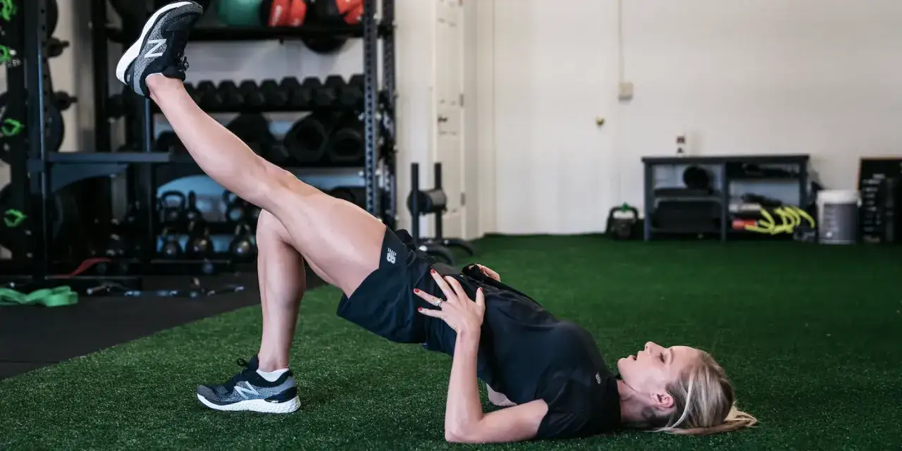 Femme faisant un pont fessier sur gazon synth&eacute;tique, un exercice cl&eacute; pour le renfo course &agrave; pied.