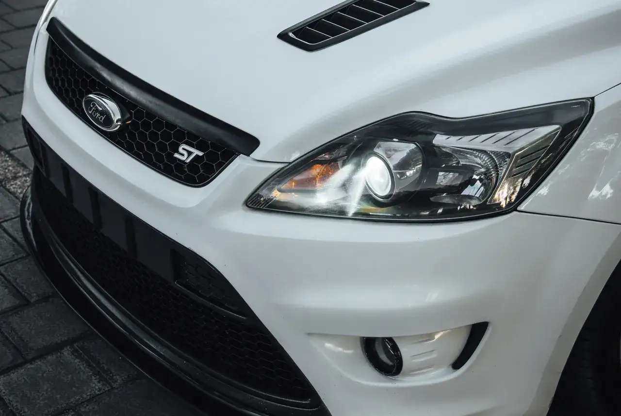 Reflektor bi-ksenon w białym Fordzie Focus ST. Jasne światło rozświetla drogę, pokazując, co to bi-ksenon.