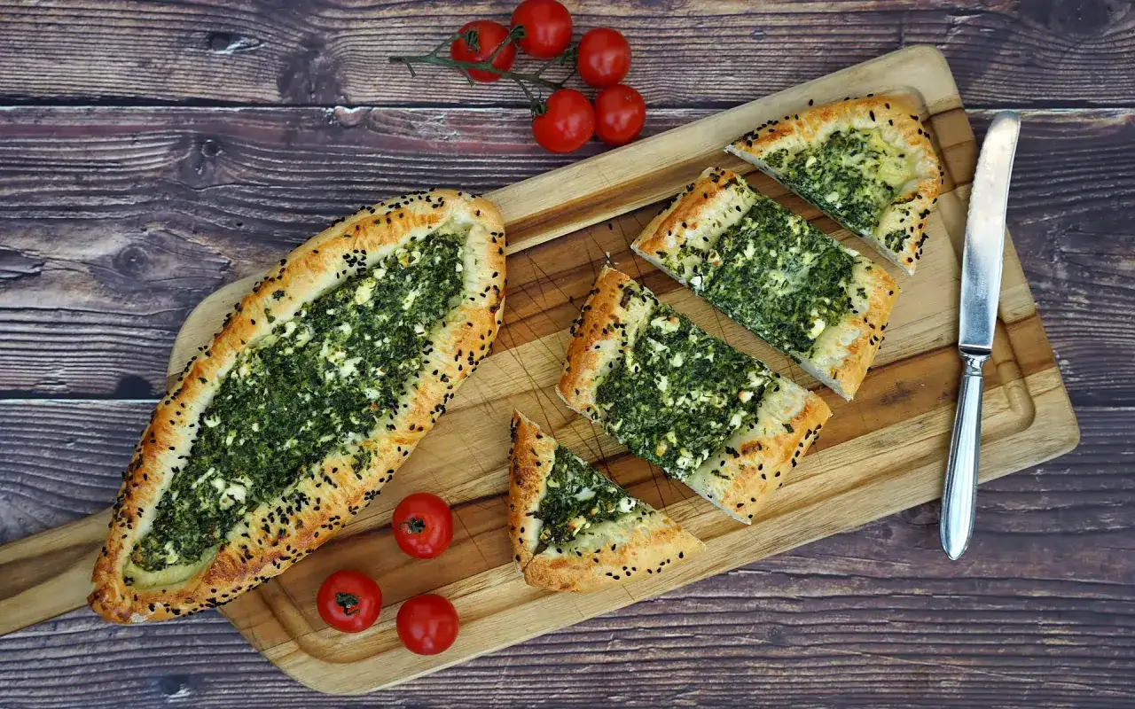 Ein leckeres Pide Rezept mit Spinat und Feta, garniert mit schwarzen Sesamk&ouml;rnern. Daneben liegen frische Kirschtomaten.