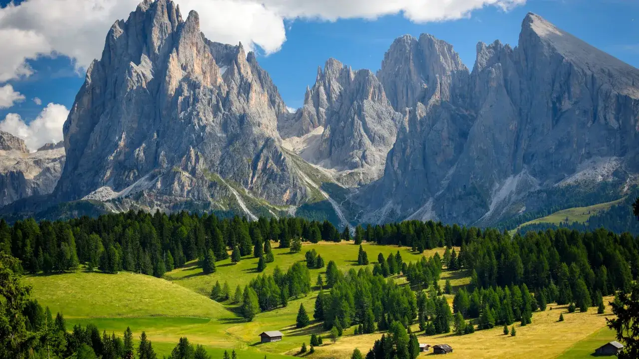 Majestic peaks of the Dolomites rise above rolling green meadows dotted with trees and small chalets. A stunning contrast to other Alps.