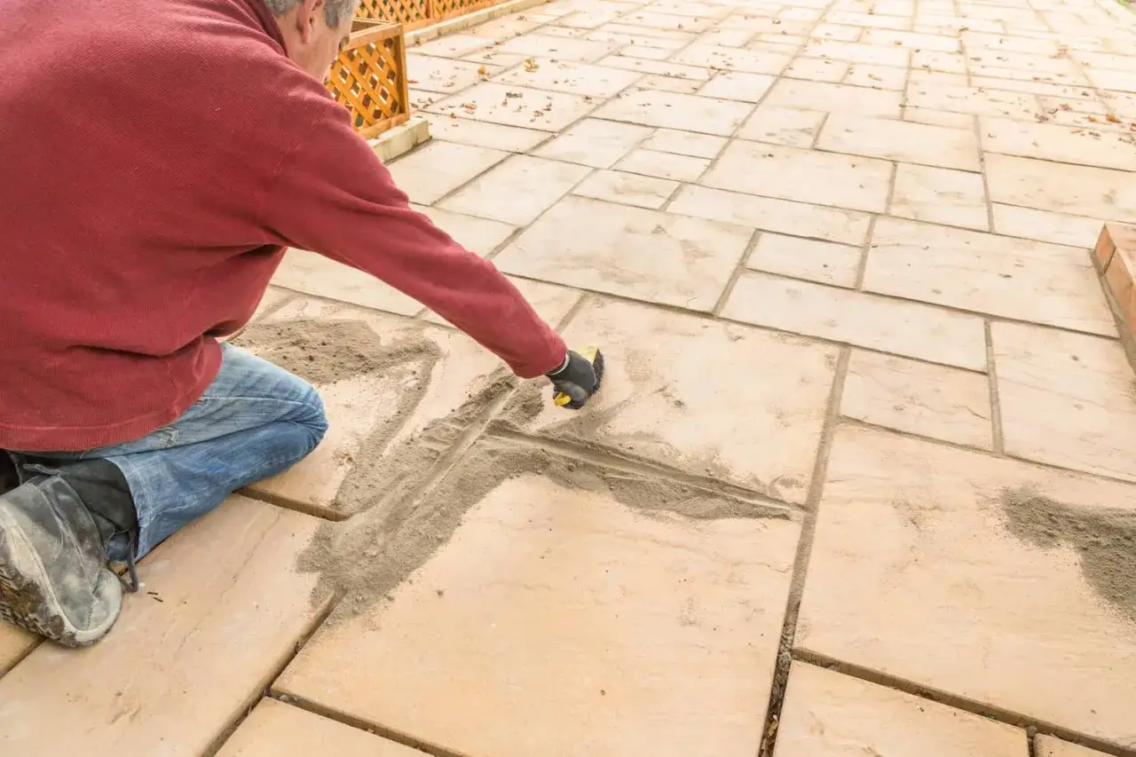 Mann kniet und verfugt Pflastersteine mit Sand.