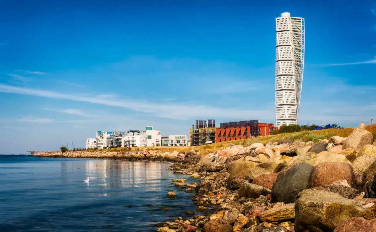 Turning Torso skyskrapan reser sig mot en klarblå himmel. En vacker utsikt över Malmös kustlinje med moderna byggnader och steniga stränder.